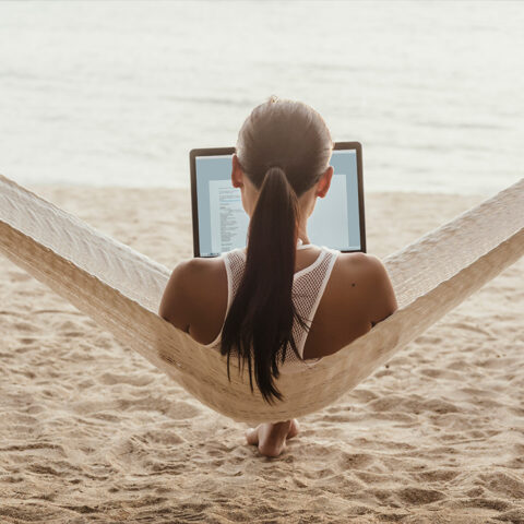 Laptop user sitting in hammock on the beach