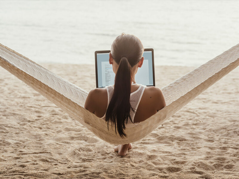 Laptop user sitting in hammock on the beach