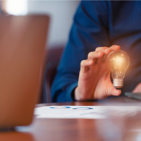 A worker sitting in front of a laptop and holding a lightbulb in his right hand