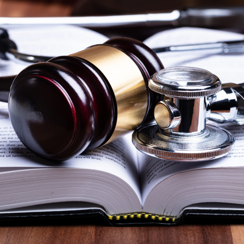 A wooden gavel and a metal stethoscope lying side by side on an open book with visible text on the pages.