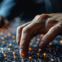 two hands hover over a table, which is covered in interconnected circuits. Some of the circuits are lit up orange.